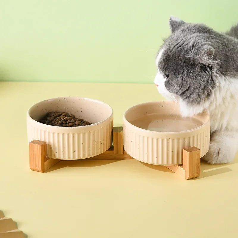 Cat drinking from premium ceramic pet food and water bowls on wooden stand by Paw Care USA